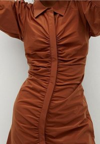 Bruine jurk met plooien, gemaakt van gladde stof, voorzien van een kraag, verticale plooien en korte pofmouwen, met een aansluitend silhouet en zijdetails.