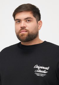Schwarzes Kurzarm-T-Shirt mit rundem Halsausschnitt. Mit weißem Logo-Text im linken Brustbereich. Aus weichem Baumwollmaterial mit glatter Textur.