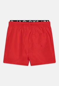 Pantaloni da bagno rossi con una vita elastica e una banda logata nera. Comprendono una tasca posteriore e un tessuto leggero e liscio.