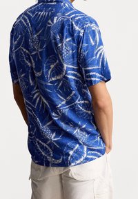 Koszula z krótkim rękawem, niebieska w biały wzór tropikalnych liści i ananasów, bawełniany materiał, luźny krój, zaokrąglony dół.