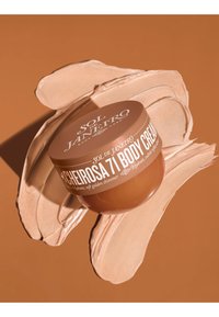 Récipient de crème pour le corps Sol de Janeiro Cheirosa 71 sur des échantillons de crème pour le corps beige crème sur fond marron assorti.