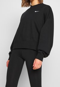 Svart sweatshirt med rundad hals, långa ärmar och en kortad design. Har en vit Nike-logotyp på vänster bröstområde.