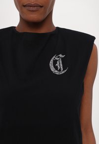 Mustat hihattomat paidat, jotka on valmistettu pehmeästä kankaasta ja joissa on kristallikoristeinen logo vasemmassa rinnassa. Yksinkertainen, sulava pinta.