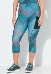 Blauwe en teal patroon capri leggings met een hoge taille, met geometrische ontwerpen. In combinatie met grijze sportschoenen met teal accenten.