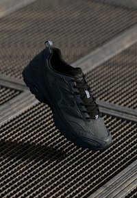 Black athletic shoe with mesh and synthetic upper, textured design, round toe, padded collar, and contrasting laces on a textured surface.