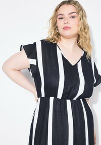Černobíle pruhované šaty s výstřihem do V, krátkými rukávy a nařaseným pasem. Vyrobené z lehké, strukturované látky.