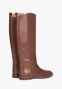 Brązowe skórzane kozaki za kolano o gładkim wykończeniu, zaokrąglonym czubku i niewielkim obcasie. Posiadają unikalny falbaniasty brzeg u góry oraz minimalne przeszycia.