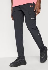 Μαύροι cargo παντελόνια από ελαφρύ ύφασμα, με πολλαπλές τσέπες, ελαστικά μανσέτες και αντανακλαστικές λεπτομέρειες. Συνδυάζονται με μαύρα αθλητικά παπούτσια.