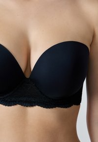 Reggiseno push-up nero con coppe in tessuto liscio e dettagli in pizzo lungo la fascia, caratterizzato da un design senza cuciture e una finitura opaca.