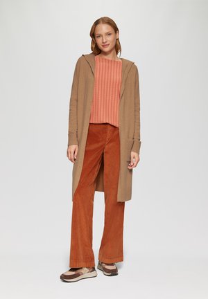 Beige cardigan met capuchon over een koraal gestreepte top, gecombineerd met rustkleurige corduroy broek en bruin-beige sneakers.