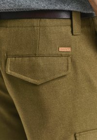Olijfgroene textuur stof cargo broek met een achterzak die een gespitse flap heeft en een klein tanleren logo patch.