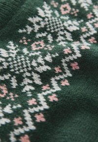 Grønt strikket stof med et fair isle mønster i hvid og blød lyserød, med geometriske former og blomstermotiver for et struktureret udseende.
