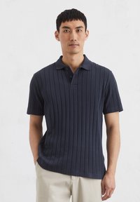 Marineblauwe geribbelde polo met korte mouwen, voorzien van een klassieke kraag en een placket met twee knopen, gemaakt van textiel met een textuur.