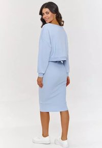 Jasnoniebieski, krótki sweatshirt z długimi rękawami, zestawiony z dopasowaną sukienką midi w pasującym prążkowanym materiale. Białe sneakersy dopełniają stylizację.