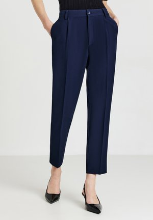 Pantaloni da cerimonia blu con pieghe, chiusura a bottone, tasche laterali e gambe affusolate. Abbinati a scarpe nere con tacco alto. Tessuto dalla texture liscia.