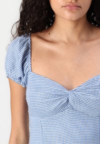 Blå och vit rutmönstrad klänning med puffärmar, hjärtformad halsringning och samlad detalj vid bysten. Slät tygkvalitet.