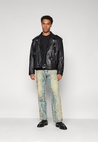 Svart skinnbikerjakke med sølvglidelåser, kombinert med lyseblå slitte jeans. Svarte sko fullfører antrekket.