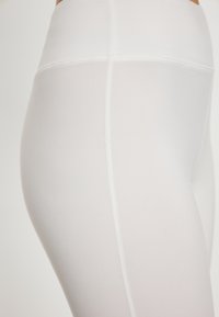 Witte leggings van lichtgewicht, rekbaar materiaal met een hoge tailleband, kenmerken vlakke naden en een gladde, matte textuur.