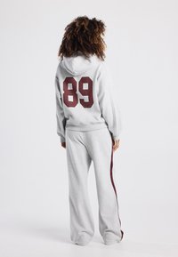 Grey hoodie and sweatpants set featuring a large maroon "89" on the back, with side stripes in maroon, made from soft fabric.