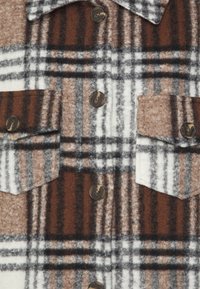 Veste en laine à carreaux marron, blanc et gris vue de face, avec quatre boutons marron, deux poches à rabat et un col pointu.