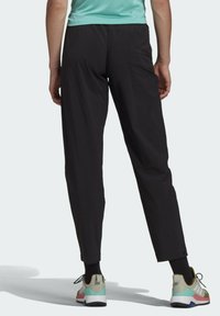 Pantalones negros, ligeros y con un corte ajustado. Cuentan con una cinturilla flexible y un bolsillo lateral. Combinados con zapatillas deportivas de colores múltiples.