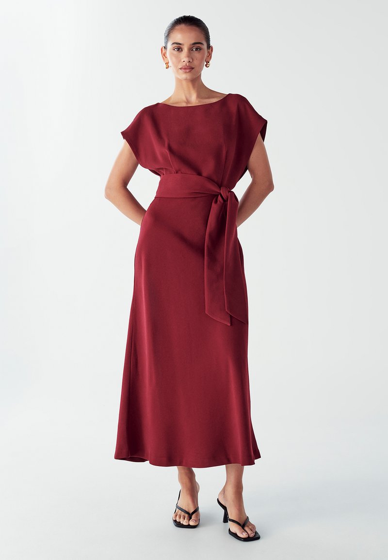 Bordo mekko, joka ulottuu nilkkoihin, löysällä istuvuudella, lyhyillä hihoilla ja vyötäröhihnalla. Silkkinen kangas, jossa on hieno kiilto ja levenevä hame.