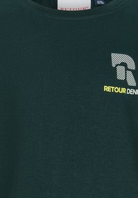 Dunkelgrünes T-Shirt mit einem weißen und gelben RETOUR DENIM-Logo und einem stilisierten "R"-Design auf der Brust.