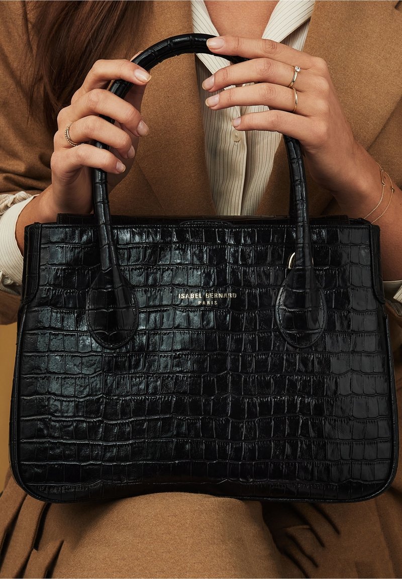 Bolso de mano de cuero negro con relieve de cocodrilo, con un diseño estructurado, equipado con dos asas redondeadas y detalle de marca en dorado.