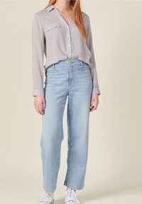 Jasnoszara koszula z długim rękawem z małymi wzorami, zestawiona z jasnoniebieskimi spodniami z szerokimi nogawkami i białymi trampkami. Koszula posiada kołnierzyk i zapięcie na guziki.