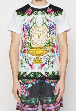 Schwarz-weißes Kurzarmhemd mit buntem Blumenmuster, das ein goldenes Emblem zeigt, und schwarze Shorts mit passenden Designelementen.