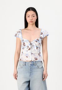 Blusa a stampa floreale con maniche corte a sbuffo, dettaglio con fiocco frontale e accenti blu chiaro. Il materiale sembra leggero e presenta una finitura testurizzata.