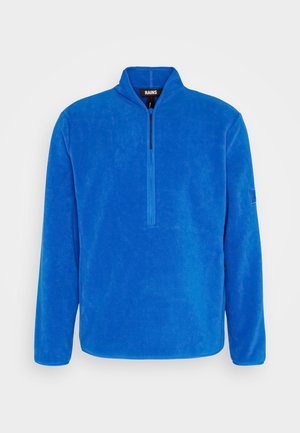 Pull polaire bleu à manches longues avec une courte fermeture éclair devant et un petit col montant, étiqueté RAINS à l’intérieur du cou.