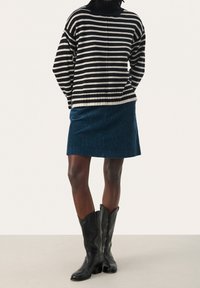 Suéter de punto a rayas blanco y negro con cuello alto, combinado con una falda de pana de color azul oscuro y botas de cowboy negras hasta la rodilla.