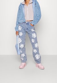 Jasnoniebieska bluza z kapturem z polaru, beżowa bluza zapinana na zamek, niebieskie dżinsy z białą kwiatową haftem, różowe buty na platformie i jasnoniebieska torebka.