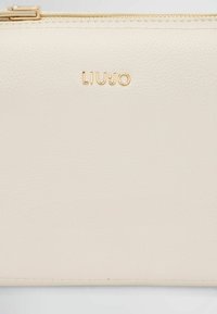 Clutch in pelle testurizzata beige chiaro con logo "LIUJO" impresso in oro; presenta una chiusura con zip e cuciture fini lungo i bordi.