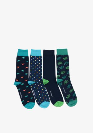 Man wearing white shorts and navy blue socks with colorful polka dots and turquoise accents, standing against a white background.