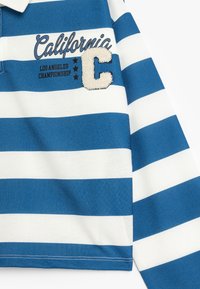 Blå och vit randig långärmad polo-tröja med broderad "California" och "C"-patchar, med olika sömnadsdetaljer.