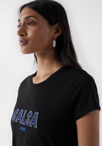 Schwarzes T-Shirt mit einem "SALSA"-Logo, verziert mit blauen und silbernen Strasssteinen, kurzen Ärmeln und einem runden Halsausschnitt.