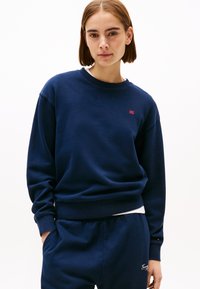 Navyblauwe sweatshirt van zacht materiaal met een ronde hals, ribbelboorden en een klein rood logo-accent op de borst. Heeft een relaxed fit.