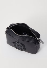 Musta nahkainen pussi, jossa on kuvioitu pinta, vetoketjukiinnitys ja toisella puolella painettu logo. Sisäpuoli on vuorattu tummalla kankaalla.