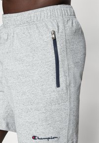 Gray knit shorts with an elastic waistband, featuring a navy zipper pocket and embroidered "Champion" logo in red and blue.