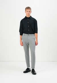 Chemise noire à boutons avec col, pantalon gris ajusté et chaussures noires. Tissu lisse, coupe fitted et sans motifs visibles.