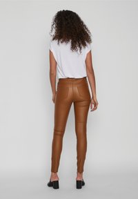 Hnědé úzké kalhoty z umělé kůže s vysokým pasem, zadními kapsami a hladkou texturou, doplněné o bílý krátký rukáv.