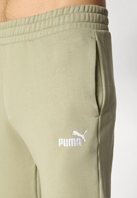 Svetlo olivovo zelené tepláky s elastickým pásom a bočnými vreckami. Na ľavom stehne sa nachádza biele vyšívané logo "PUMA". Mäkký materiál z bavlnenej zmesi.