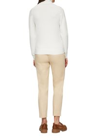 Pull en tricot blanc avec un col montant, associé à un pantalon moulant beige clair et des chaussures marron, vu de dos.