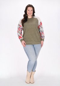 Olivově zelený žebrovaný svetr s květinovým vzorem a vícebarevnými rukávy. Kombinujte s světle modrými skinny džíny a béžovými kotníkovými botami.