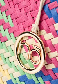 Gevlochten, meerkleurige tas met roze, groene, blauwe en crème draden, met een gouden, ronde label met de merknaam "nobo."