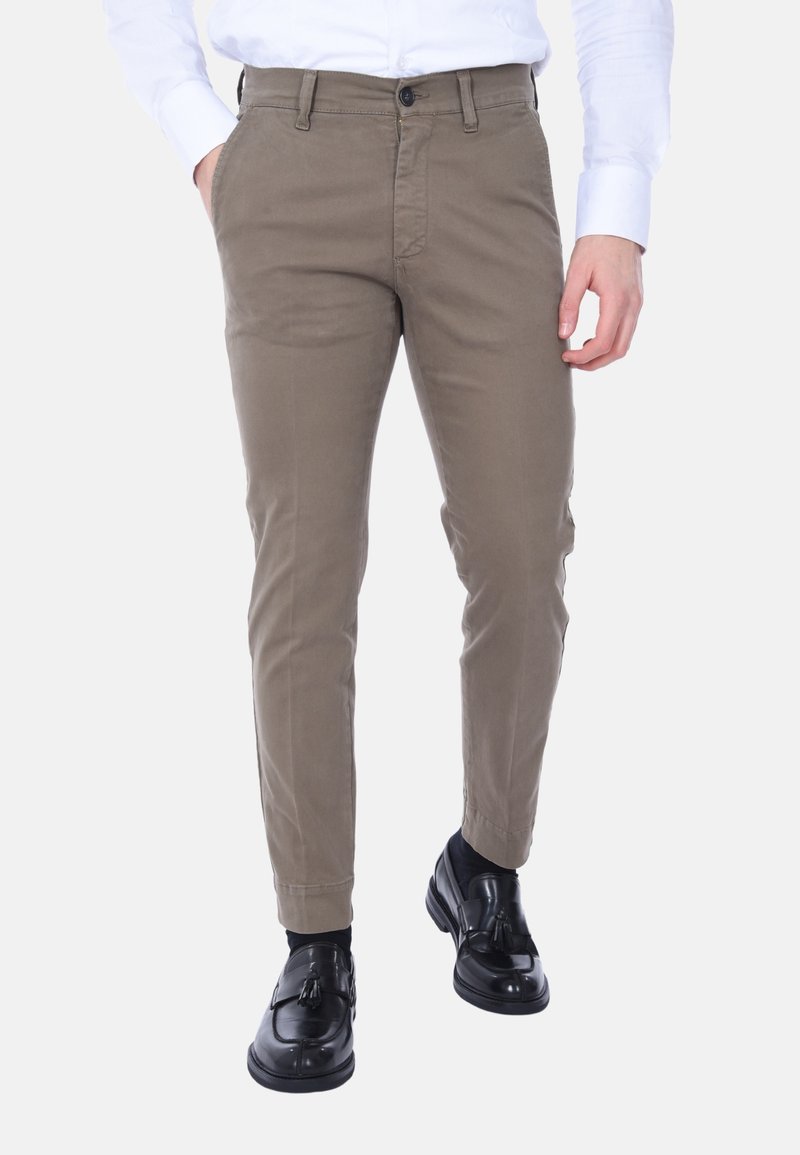 Chinos in cotone beige con una vestibilità slim, caratterizzati da chiusura con bottone, cinque tasche e gambe affusolate. Indossati con scarpe eleganti nere.
