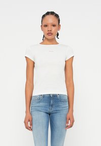 Tricou alb ajustat, cu mâneci scurte și decolteu rotund; prezintă un mic logo roșu pe piept; asortat cu blugi blue.