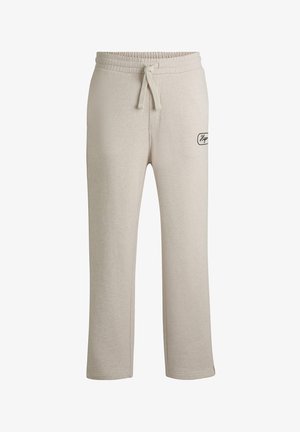 Pantalons de survêtement beiges avec une coupe décontractée, taille élastique, cordon de serrage et poches latérales. Présente un petit patch logo noir sur la cuisse.